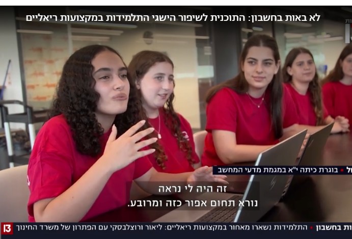 A screenshot of Channel 13 news. A team of 5 girls sit side by side, with two laptops in front of them. The girl closest to the camera is explaining QueenB's impact to someone off-screen.