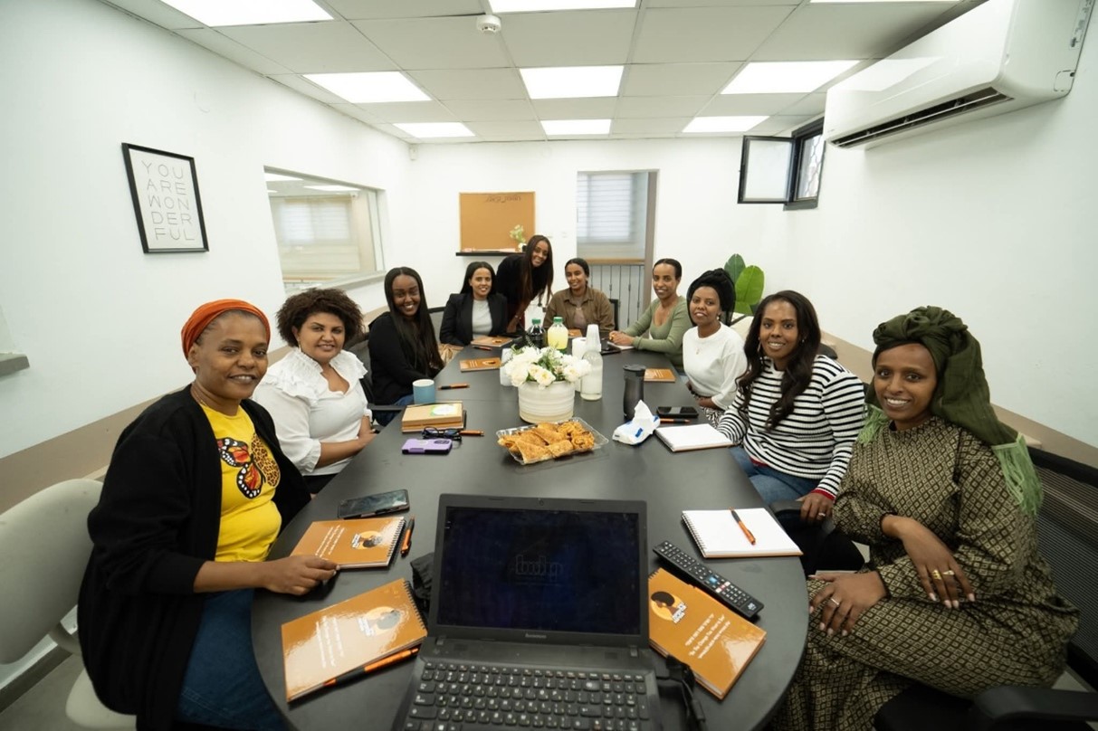 Empowering Ethiopian Women shared photo 10 Participants at a workshop run by Empowering Ethiopian women. The women, smiling towards the camera, are seated at a table with workbooks in front of them.