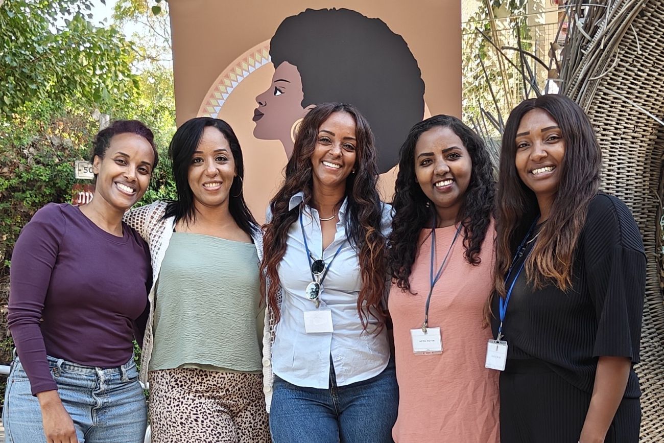 10 Participants at a workshop run by Empowering Ethiopian women. The women, smiling towards the camera, are seated at a table with workbooks in front of them.